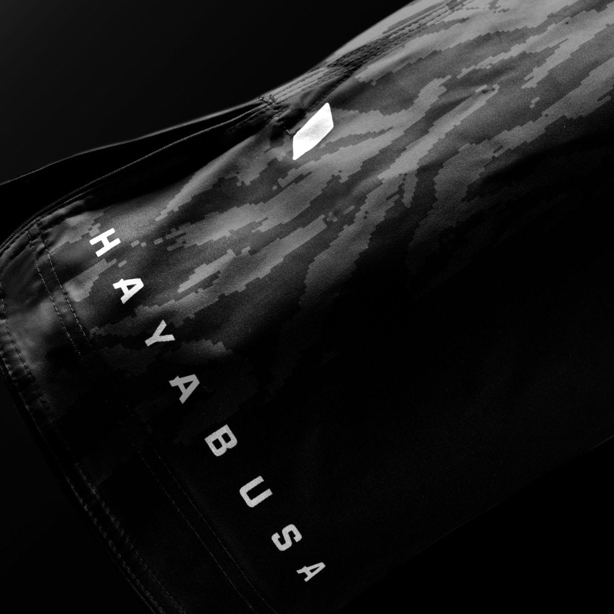 Detalle en primer plano de la escritura de la marca Hayabusa en la pernera de los pantalones cortos negros Apex 3/4