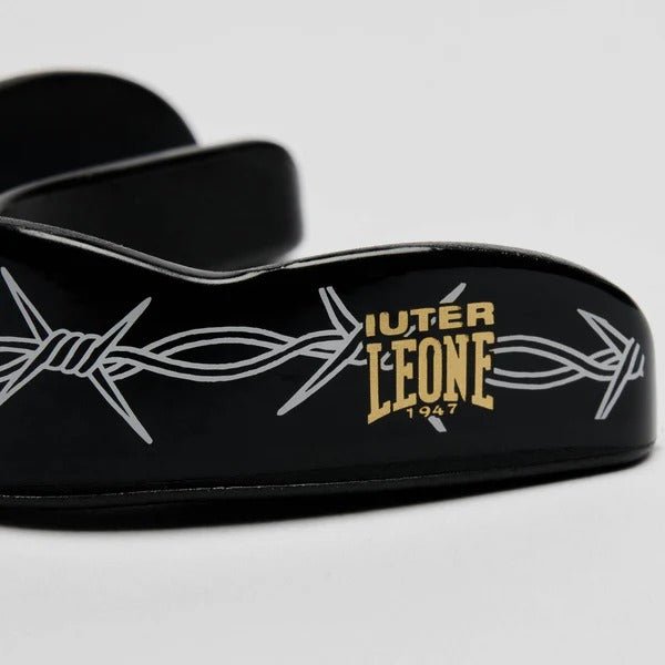 Detalle en primer plano del logotipo dorado de LEONE x IUTER y gráficos de alambre de púas