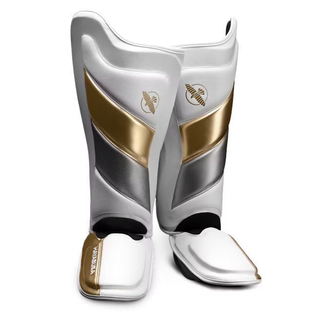 Par de espinilleras Hayabusa T3 Striking blancas y doradas para kickboxing y MMA, vista frontal