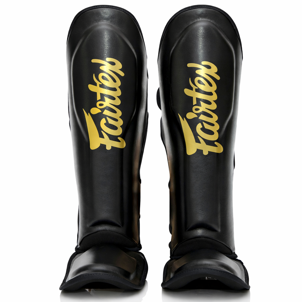 Espinillera FXB Fairtex versión bicolor en negro y dorado con logotipos de marca compartida