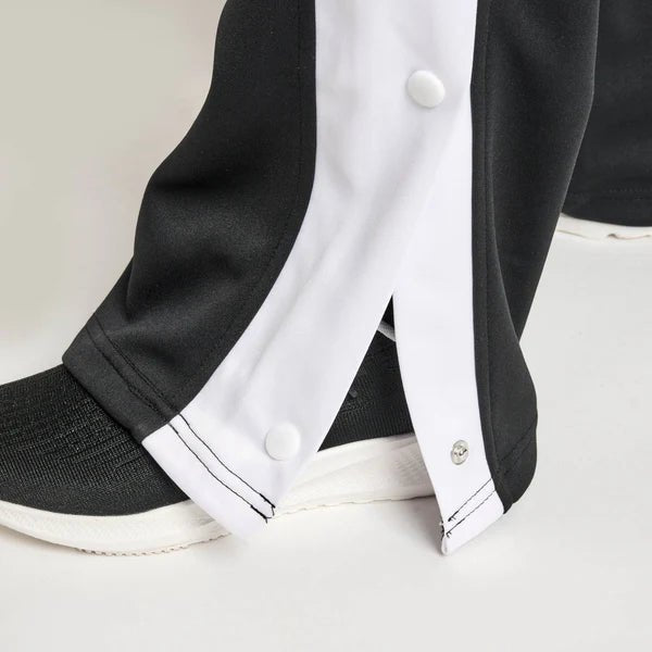 Detailní záběr na postranní odtrhávací knoflíky na černých teplákách Leone Stripe