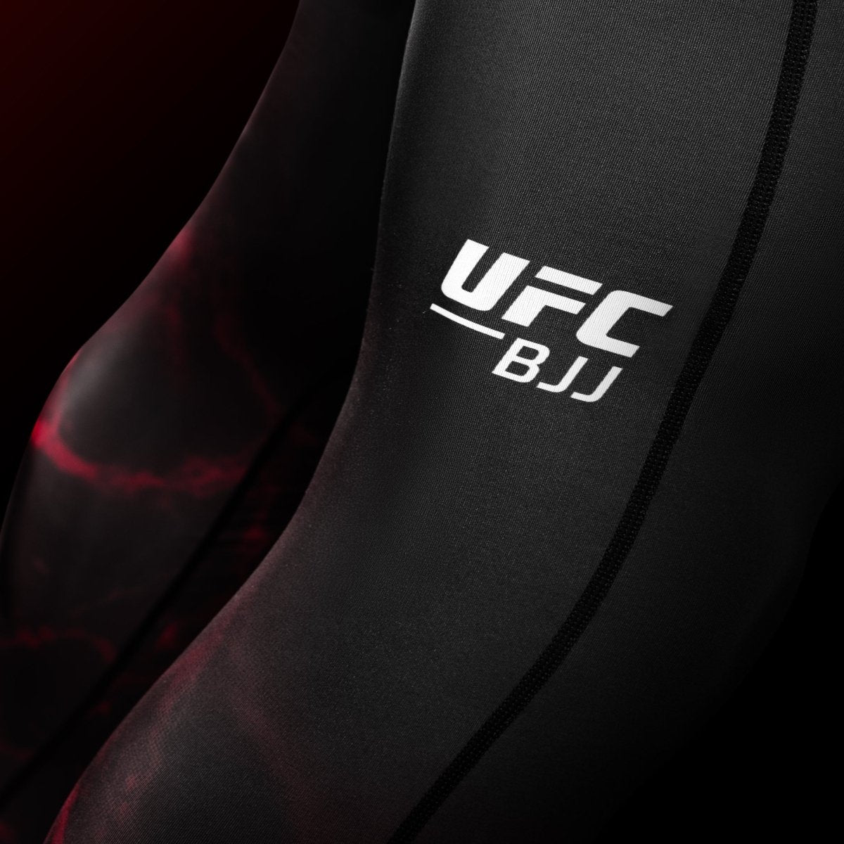 Gros plan sur le graphisme UFC sur la jambe du legging BJJ Spats noir et rouge, détail des coutures renforcées