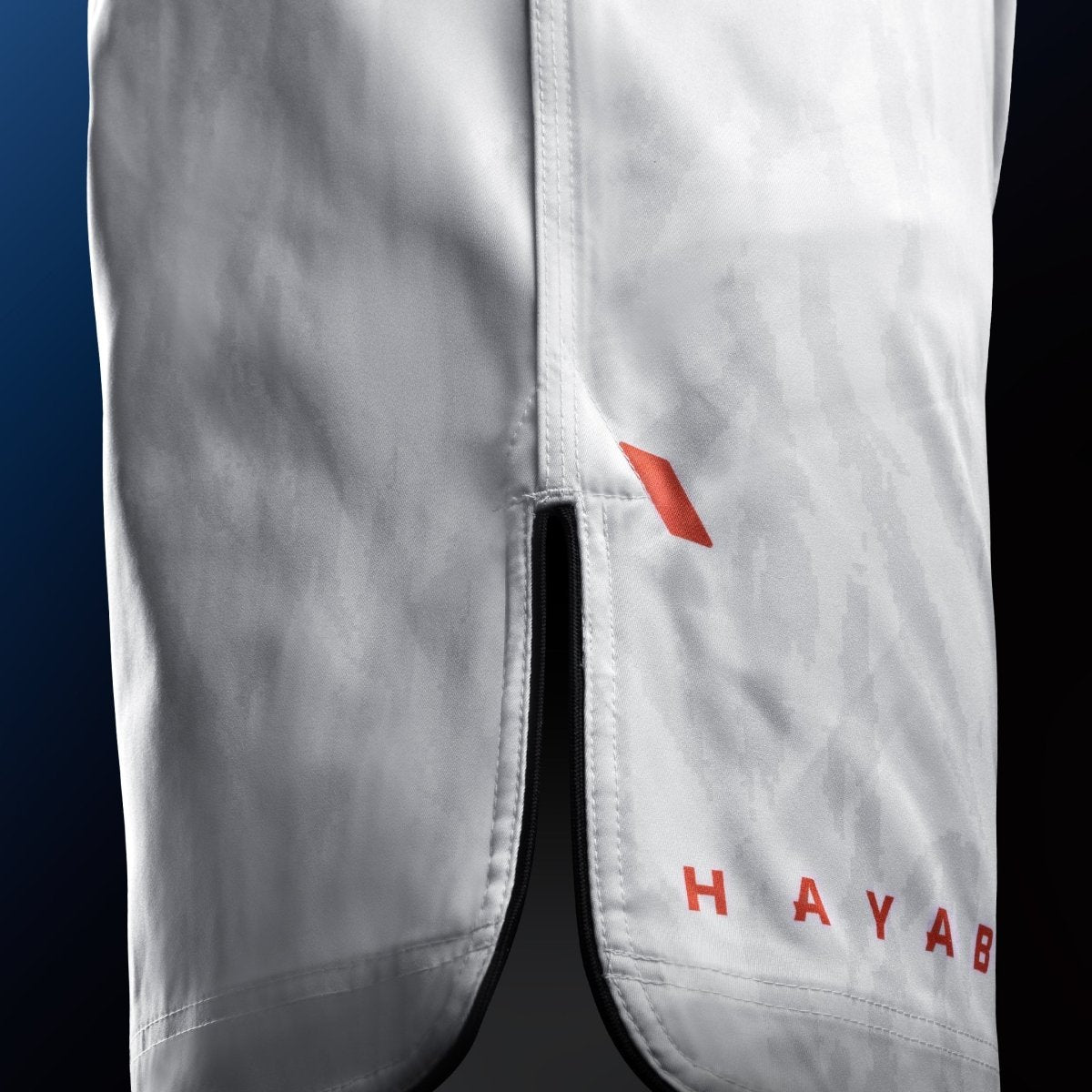 Vista lateral de los pantalones cortos blancos de MMA Hayabusa Apex a mitad del muslo con detalle de ventilación para máxima movilidad